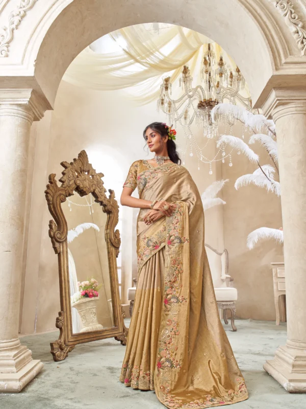 Model posing in a shimmering gold tissue silk designer saree with a heavily embroidered floral border, standing under an ornate archway in a luxurious setting.