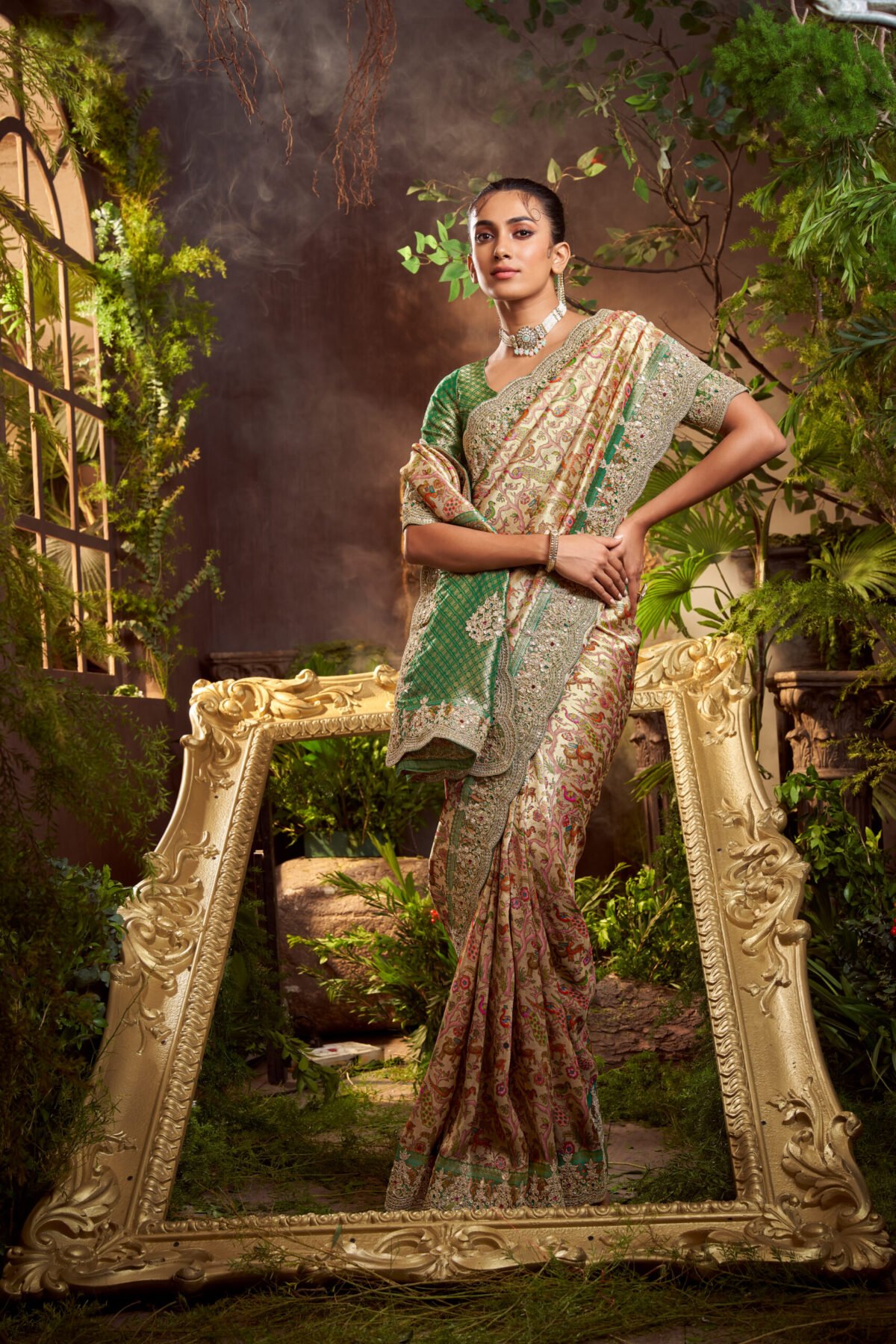 Model posing in a shimmering gold tissue silk designer saree with a heavily embroidered floral border, standing under an ornate archway in a luxurious setting.