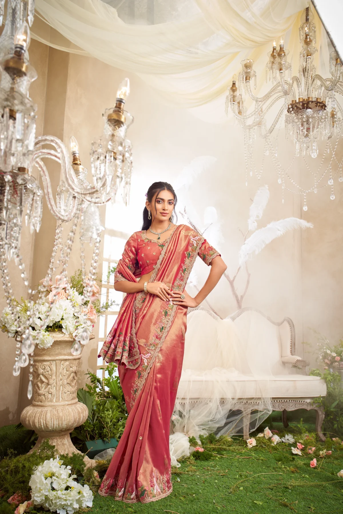 Model posing in a green and multi-color heavily embroidered designer saree, framed by a large ornate golden frame in a lush garden setting.