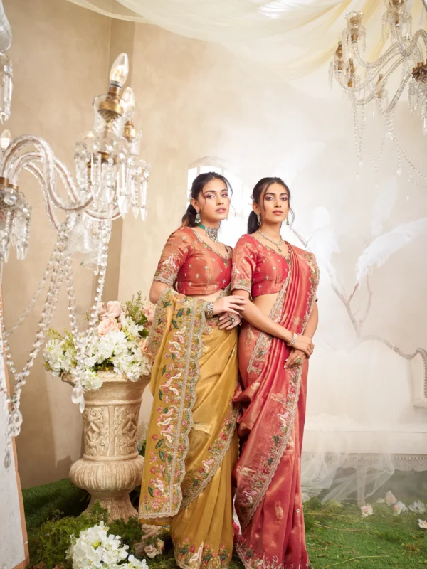 Model posing in a luxury sea green and beige designer saree with heavy floral embroidery, standing on a staircase under cherry blossoms.