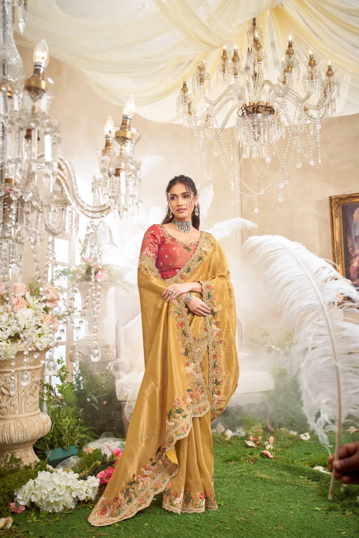 Model posing in a luxury sea green and beige designer saree with heavy floral embroidery, standing on a staircase under cherry blossoms.