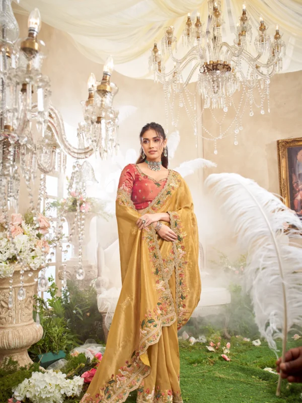 Model posing in a luxury sea green and beige designer saree with heavy floral embroidery, standing on a staircase under cherry blossoms.